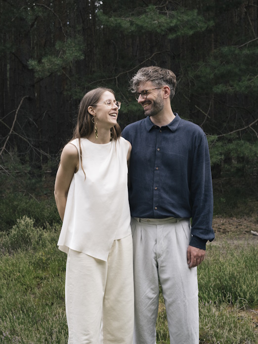 Paarfoto einer Frau in heller Leinen-Bekleidung & eines Mannes mit dunkelblauem Hemd & hellgrauer Hose