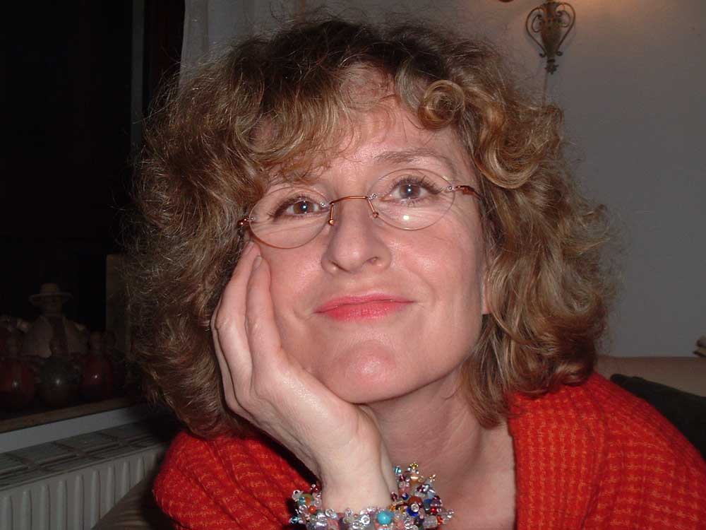 Frau mit lockigem, schulterlangen Haar, Brille und rotem Pullover